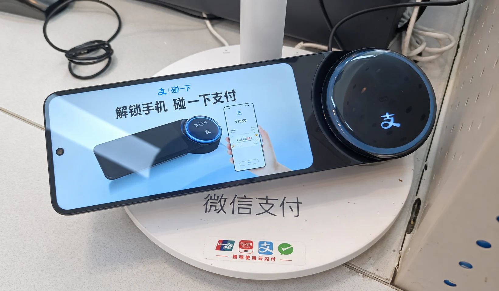 An Alipay payment terminal on a real shop counter, with payment signs below