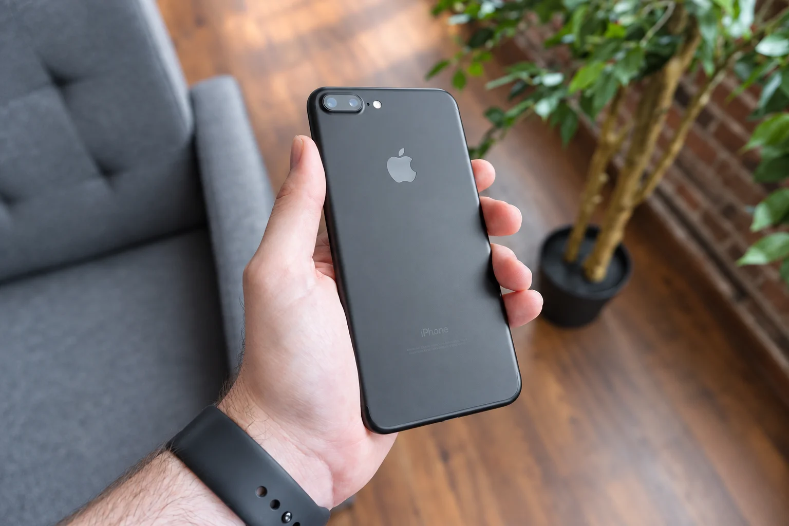 A hand holding the back of a dark smartphone, with greenery behind